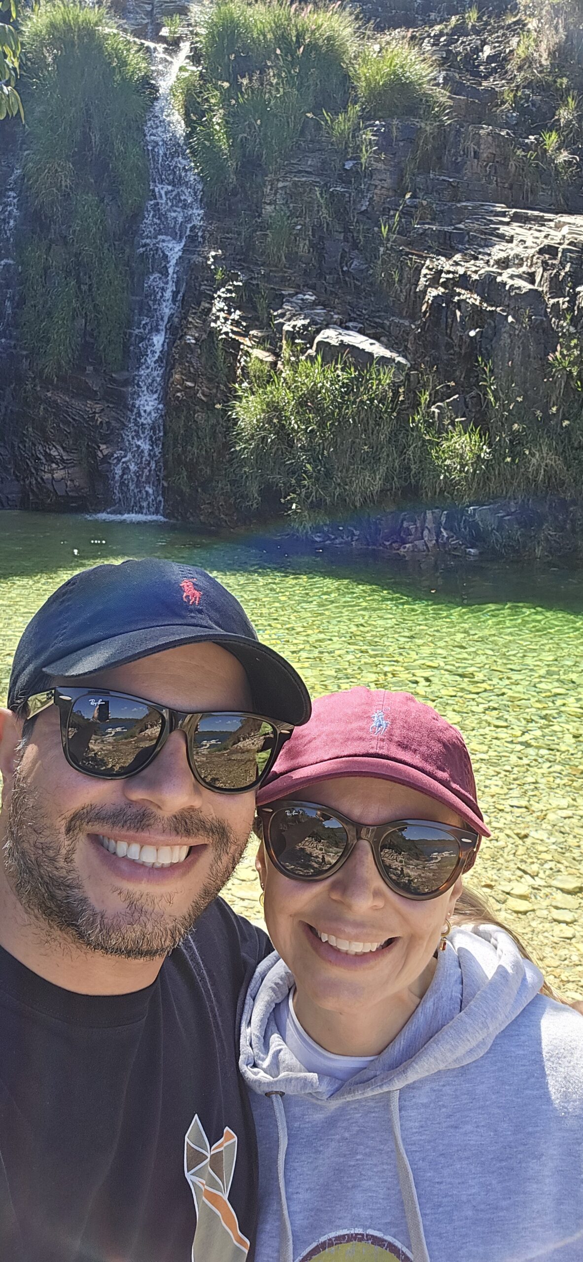 Casal em frente a cachoeira e lagoa esverdeada durante roteiro de Capitólio em 1 dia